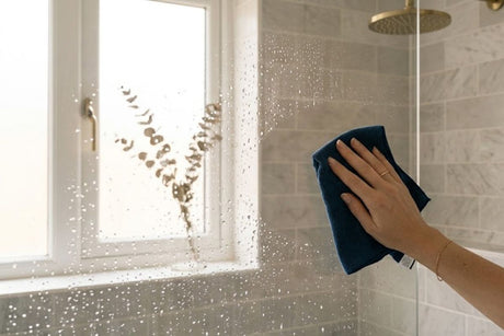 Hand cleaning wet shower glass with soft cloth